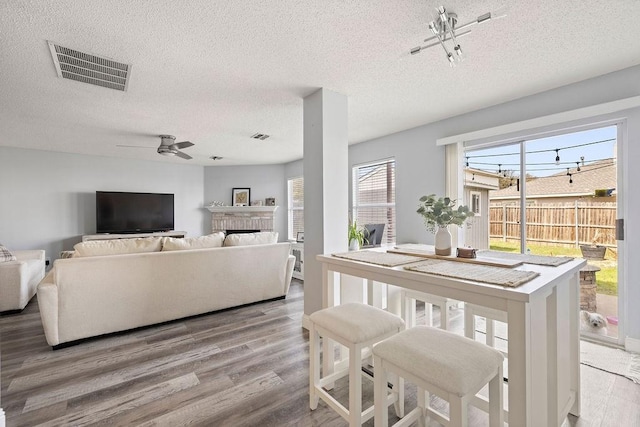 dining space featuring a fireplace, visible vents, a ceiling fan, a textured ceiling, and wood finished floors