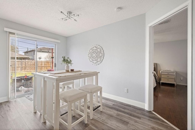 dining room featuring a textured ceiling, wood finished floors, visible vents, and baseboards