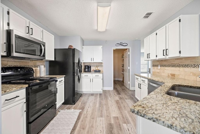 kitchen with a sink, visible vents, light stone countertops, black appliances, and light wood finished floors