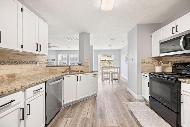 kitchen with light wood finished floors, visible vents, appliances with stainless steel finishes, a sink, and light stone countertops