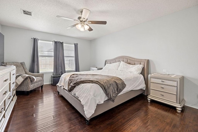 bedroom with baseboards, visible vents, a ceiling fan, dark wood-type flooring, and a textured ceiling