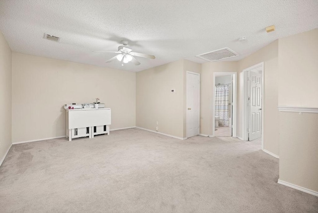 carpeted empty room with visible vents, attic access, a ceiling fan, a textured ceiling, and baseboards