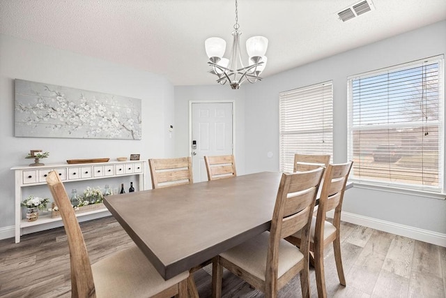 dining room featuring a notable chandelier, visible vents, light wood-style floors, a textured ceiling, and baseboards