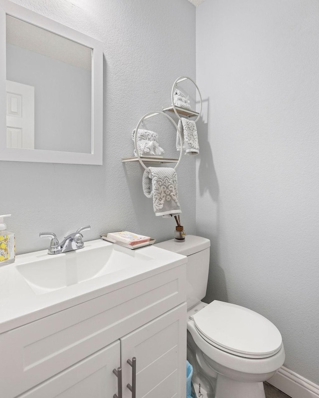 bathroom with a textured wall, vanity, and toilet