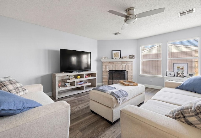 living room with ceiling fan, visible vents, a fireplace, and wood finished floors