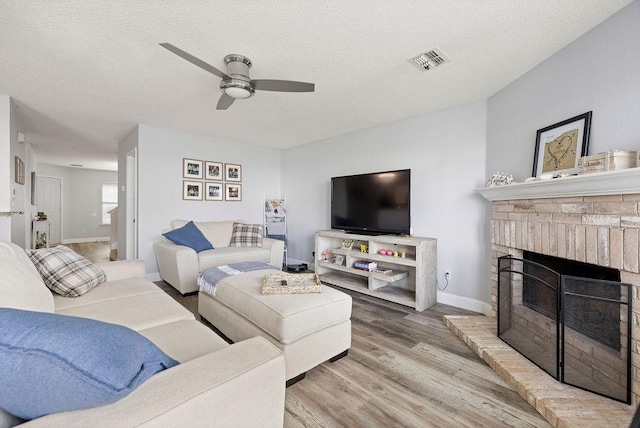 living room with a textured ceiling, a fireplace, wood finished floors, and visible vents