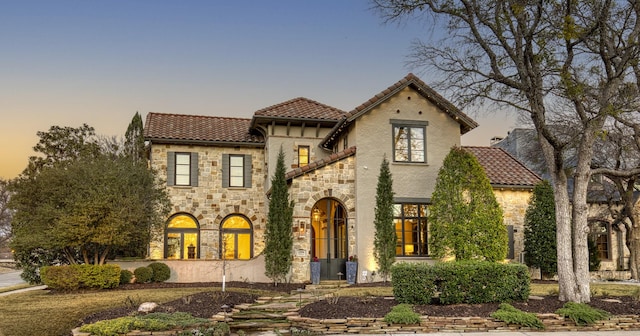 mediterranean / spanish-style home featuring stone siding, a tiled roof, and stucco siding