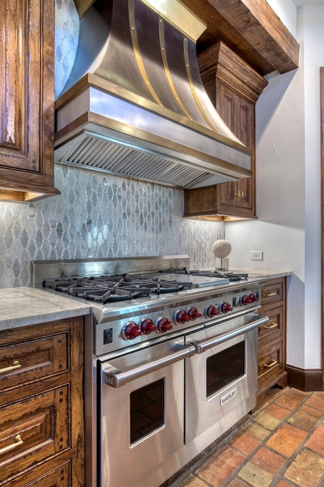 kitchen featuring tasteful backsplash, baseboards, custom range hood, light stone counters, and double oven range