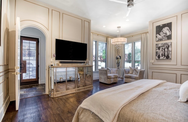 bedroom featuring arched walkways, a decorative wall, dark wood finished floors, and recessed lighting