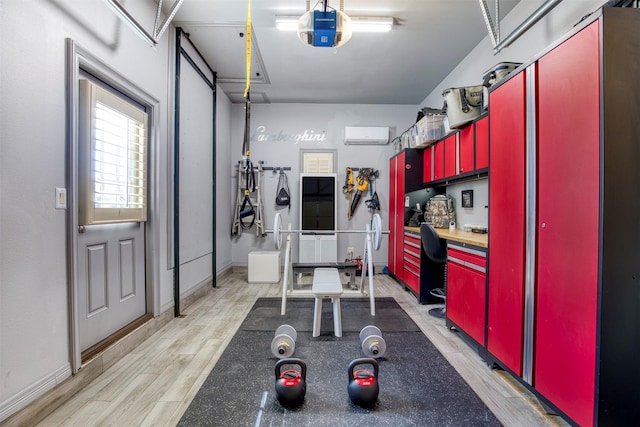 exercise room with a garage, a wall mounted air conditioner, light wood-style flooring, and baseboards