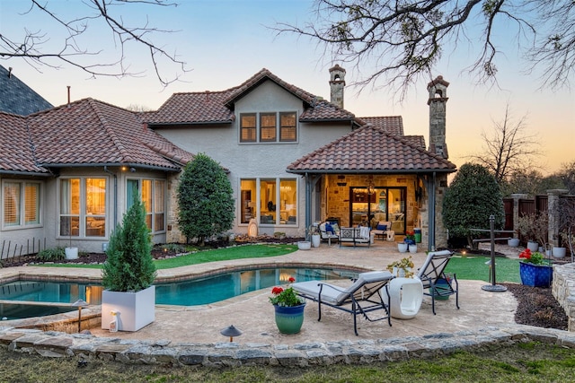 rear view of house featuring a tile roof, an outdoor living space, a chimney, a patio area, and a hot tub