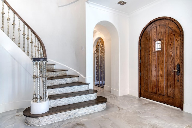 foyer featuring arched walkways, ornamental molding, stairway, and visible vents