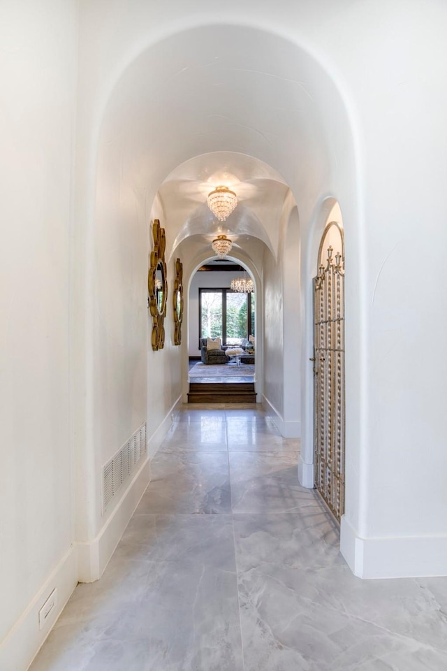 corridor with arched walkways, vaulted ceiling, visible vents, and baseboards