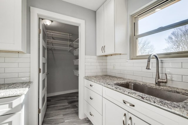 kitchen featuring decorative backsplash, light stone countertops, white cabinetry, and a sink