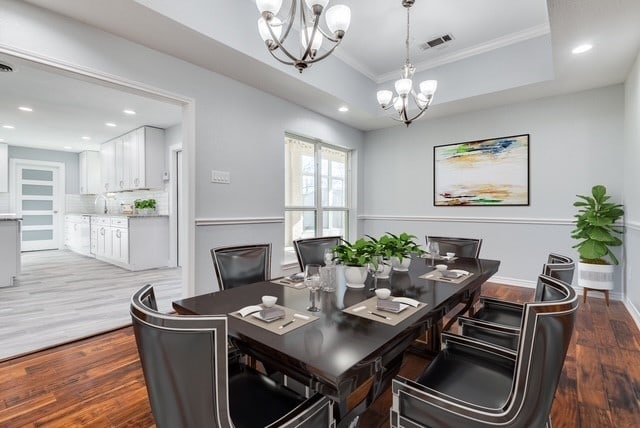 dining area featuring visible vents, a notable chandelier, light wood-style flooring, ornamental molding, and a raised ceiling