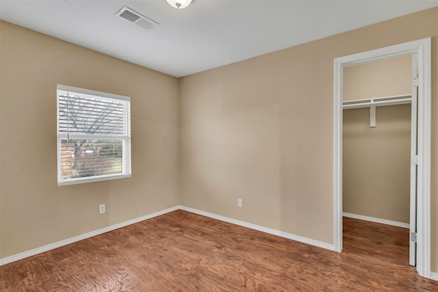 unfurnished bedroom with a walk in closet, visible vents, baseboards, and wood finished floors