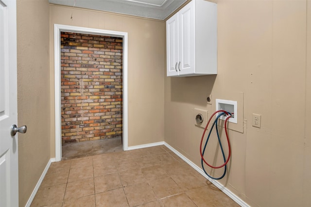 clothes washing area featuring hookup for a washing machine, hookup for an electric dryer, brick wall, baseboards, and cabinet space