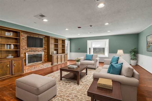 living room with built in features, a brick fireplace, wainscoting, a textured ceiling, and wood finished floors