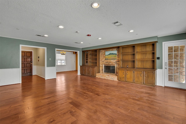 unfurnished living room featuring a wainscoted wall, wood finished floors, a textured ceiling, a fireplace, and recessed lighting