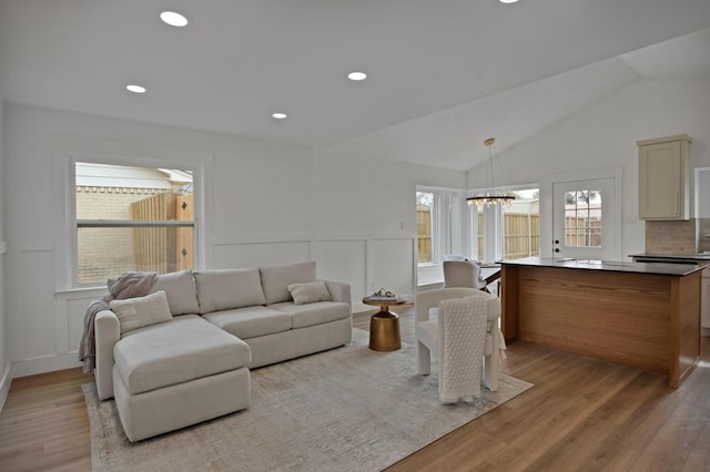 living area featuring light wood-style flooring, recessed lighting, a notable chandelier, a decorative wall, and vaulted ceiling