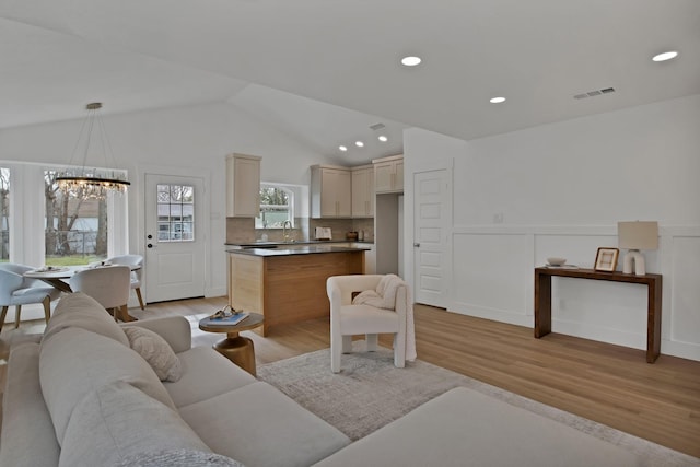 living room featuring lofted ceiling, wainscoting, visible vents, and light wood-style floors