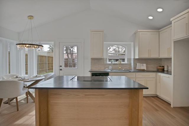 kitchen with dark countertops, light wood finished floors, vaulted ceiling, and a sink