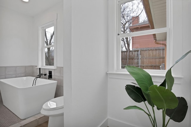 bathroom featuring a soaking tub and toilet