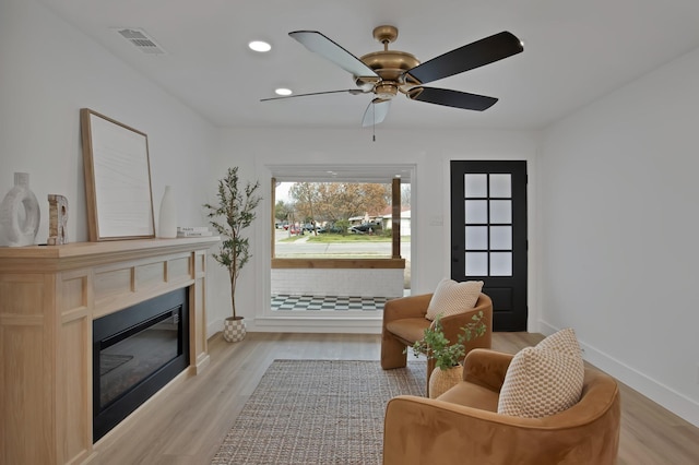 living area featuring visible vents, baseboards, a glass covered fireplace, light wood-style flooring, and recessed lighting