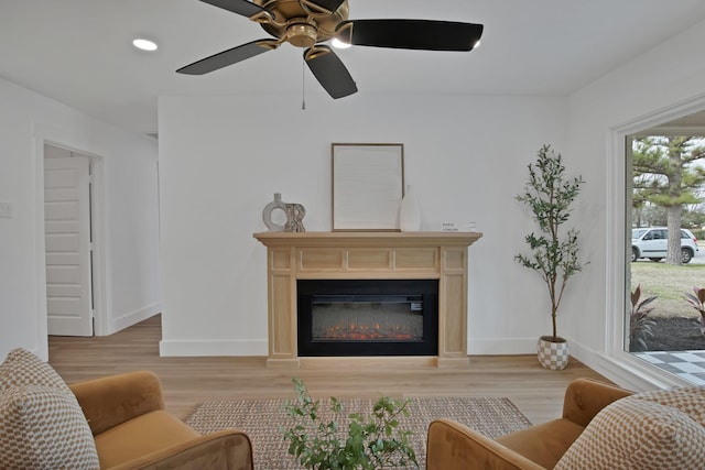 living area with recessed lighting, light wood-type flooring, a glass covered fireplace, and baseboards