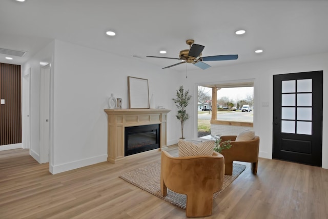 living area with visible vents, baseboards, a glass covered fireplace, light wood-style flooring, and recessed lighting