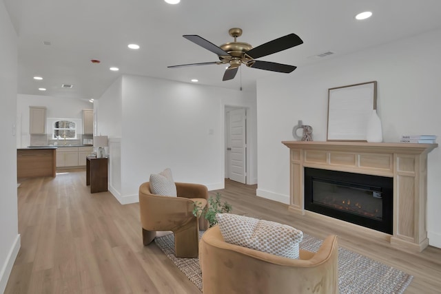 living area featuring light wood finished floors, recessed lighting, visible vents, a glass covered fireplace, and baseboards