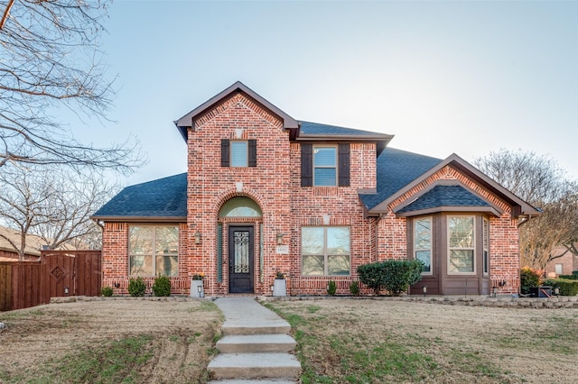 traditional-style home featuring a front yard, fence, brick siding, and roof with shingles