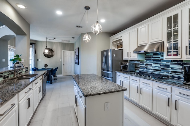 kitchen with under cabinet range hood, a sink, stainless steel appliances, arched walkways, and decorative backsplash