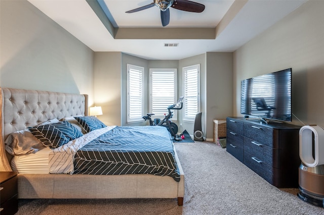 carpeted bedroom with a tray ceiling, baseboards, visible vents, and a ceiling fan