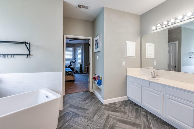 full bath with vanity, a freestanding tub, baseboards, and visible vents