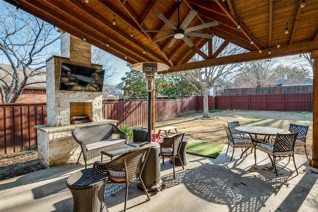 view of patio featuring ceiling fan, a gazebo, an outdoor stone fireplace, a fenced backyard, and outdoor dining space