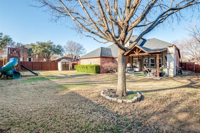 view of yard with a storage unit, a fenced backyard, an outdoor structure, and a playground