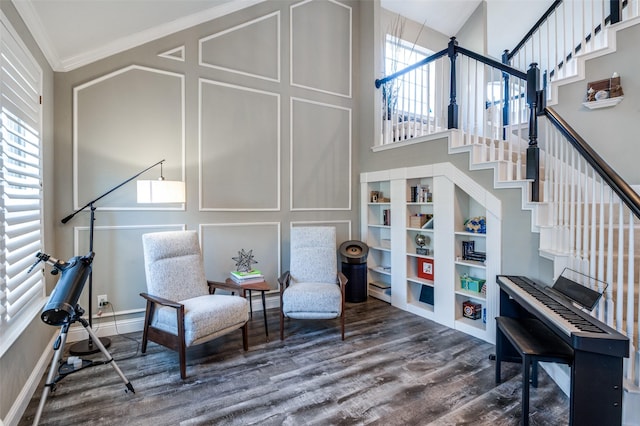 living area featuring wood finished floors, a high ceiling, stairs, crown molding, and a decorative wall