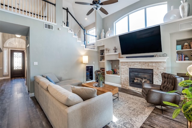 living area featuring visible vents, built in shelves, a stone fireplace, and hardwood / wood-style flooring