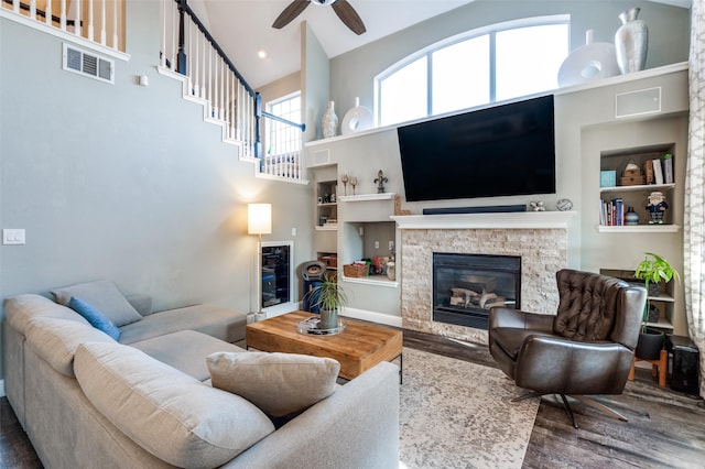 living room featuring visible vents, built in features, a stone fireplace, and wood finished floors