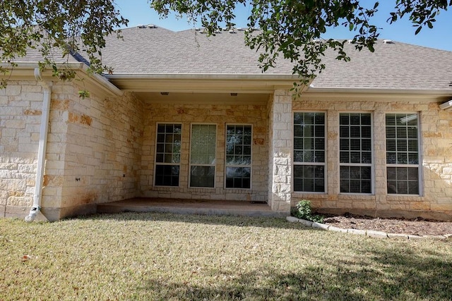 rear view of property featuring a shingled roof, stone siding, and a lawn