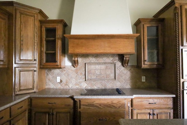 kitchen featuring brown cabinets, tasteful backsplash, custom exhaust hood, and black electric cooktop