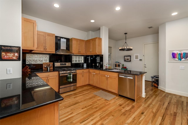 kitchen featuring a peninsula, a sink, appliances with stainless steel finishes, wall chimney exhaust hood, and dark countertops