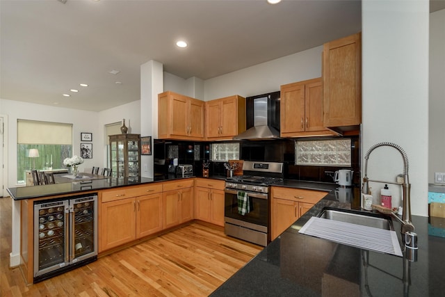 kitchen featuring beverage cooler, a peninsula, a sink, wall chimney range hood, and gas range