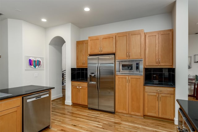 kitchen with light wood finished floors, tasteful backsplash, dark countertops, recessed lighting, and appliances with stainless steel finishes