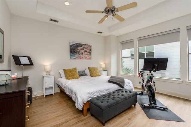 bedroom with light wood finished floors, a tray ceiling, and visible vents