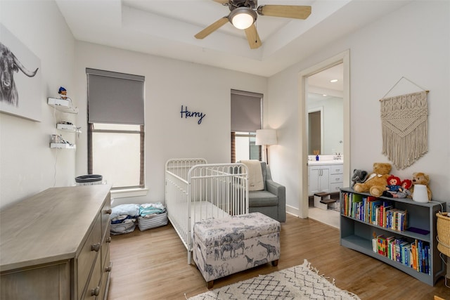 bedroom with ensuite bath, light wood-style flooring, a raised ceiling, and a ceiling fan