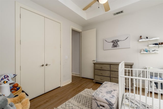 bedroom with visible vents, a ceiling fan, wood finished floors, a tray ceiling, and a closet