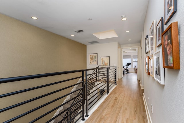 hallway with light wood-style flooring, recessed lighting, a skylight, an upstairs landing, and visible vents