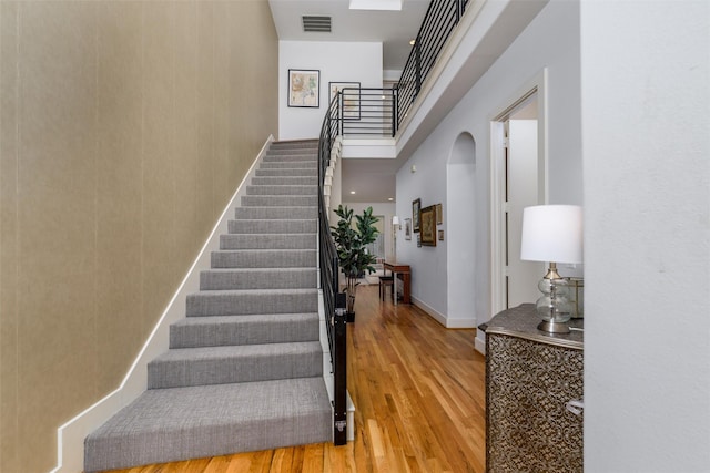 stairs featuring baseboards, visible vents, arched walkways, a towering ceiling, and wood finished floors